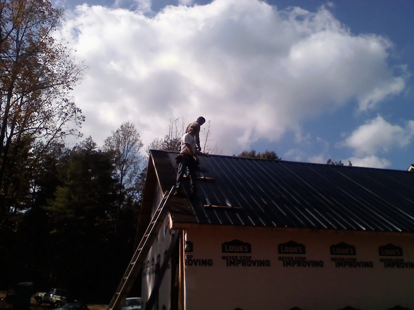 Roofer fastening dark metal panels high against a cloudy sky, from a Roof Inspection job in Auburndale