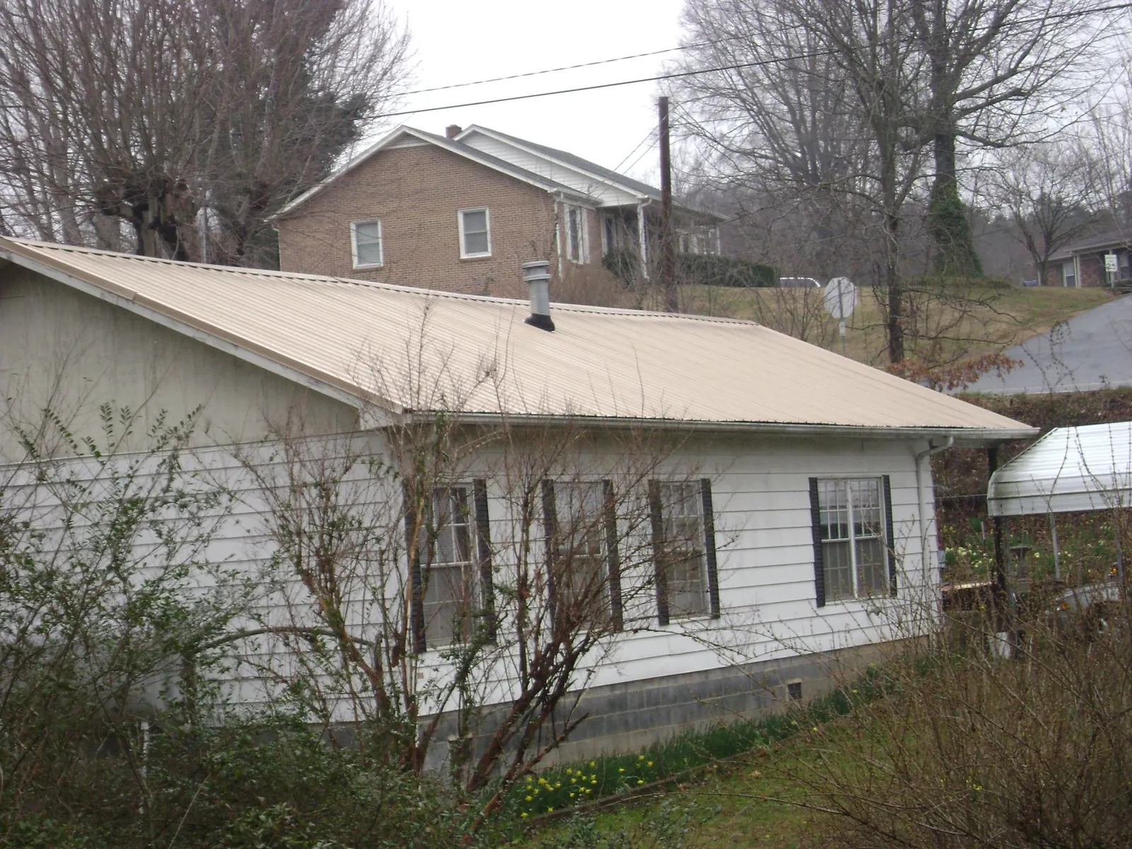 Tan metal roof on a white sided house set into a hillside — Commercial Roofing by Roofing Brothers in Auburndale