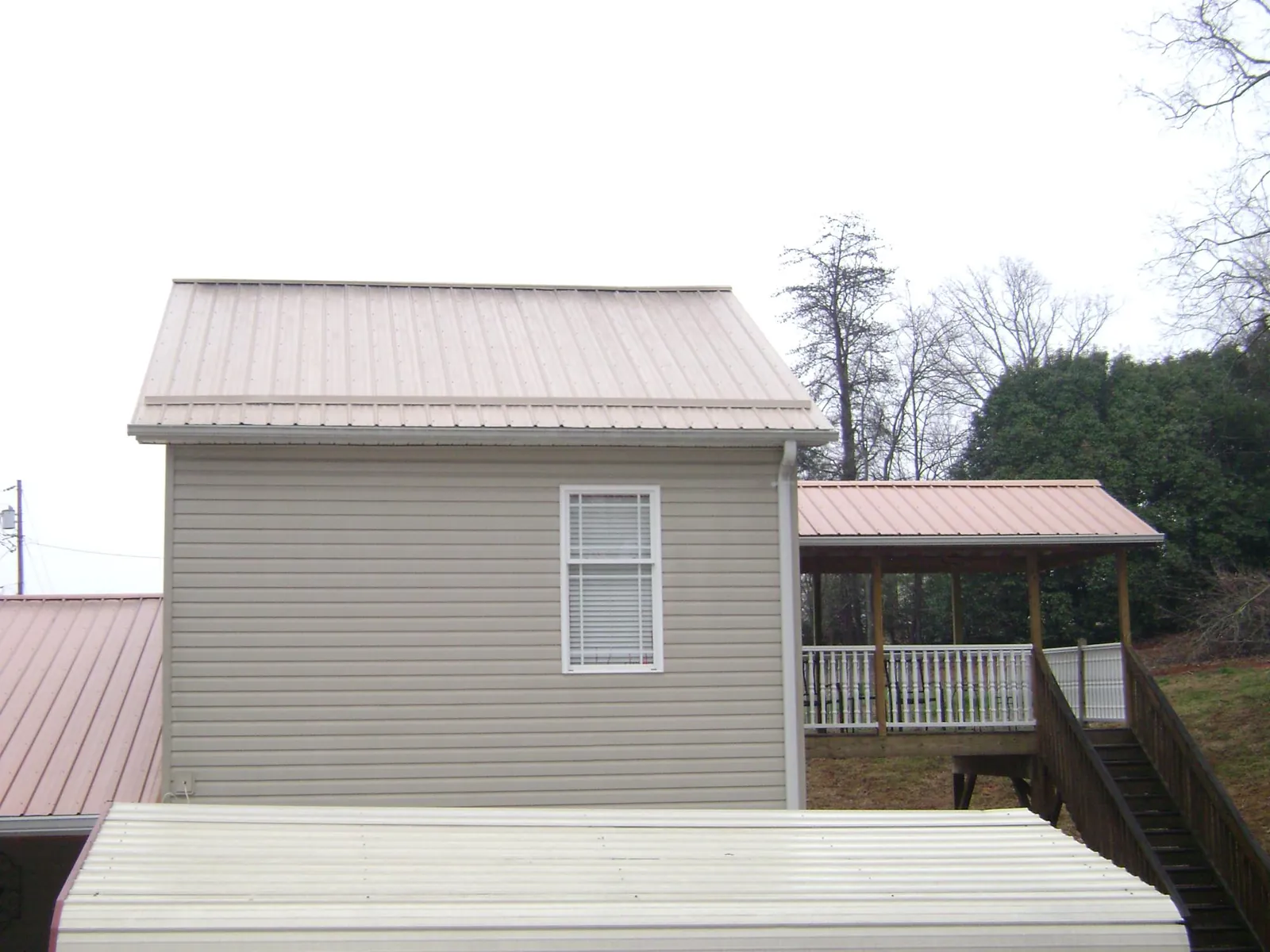 Tan metal roofs on a two story addition and attached porch, from a Roof Replacement job in Auburndale